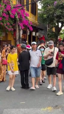 Bir grup turist caddelerde yürüyor, triportörler müşterileri bekliyor, insanlar fotoğraf çekiyor, sarı evleri görüyorlar Hoi An Şehri Vietnam 05.02.2025