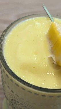 Taze yapılmış sarı turuncu ve mangolu smoothie, güneşli sarı arka plandaki bir şişeden bir bardağa akıyor. Yüksek kalite 4k görüntü
