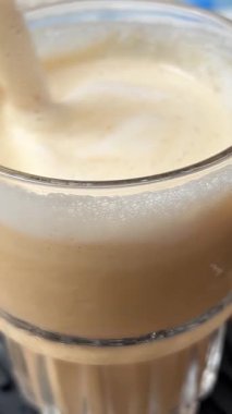 Canlı bir şehir kafesinde güneşli bir günde köpüklü kapuçinoyu karıştırmak. Süt köpüklü kahve uzun siyah bir kaşıkla karıştırılır. Kahve yapma sanatı, barista. 