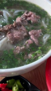 Vietnam pho çorbası aromatik et suyu, pirinç eriştesi ve taze otlar. Kültürel gelenek ve sağlıklı yemek deneyimi sergileyen lezzetleri geliştirmek için fesleğen ve limon ekleme süreci..