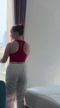 Arkadan bakan mutlu genç kadın perdeyi açıyor lüks bir dairede ya da modern bir otelde tek başına panoramik pencereden bakıyor ve sabah manzaranın keyfini çıkarıyor. Yeni konut, mülkiyet, seyahat.