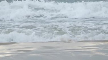 Deniz kıyısını kapatın. Sakin okyanus suyu dalgaları kumlu sahile vuruyor. Küçük mavi deniz dalgaları yaz sabahı kumsalda ağır çekimde dalgalanır. Soyut doğa arka plan seyahati rahatla.