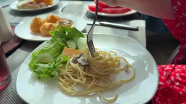 Gri tabakta çıtır pastırmalı, sebzeli ve otlu baharatlı fettuccine spagettisini döndüren yakın çekim çatalı. Yüksek kalite 4k görüntü