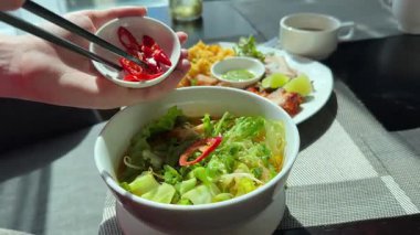 Bir kase wonton eriştesine sambal biberi sosu ekleyen biri, yemeye hazır, Endonezya sokak yemeklerinin zengin lezzetlerini ve baharatlı yemek geleneklerini yakalıyor. Yüksek kalite 4k görüntü