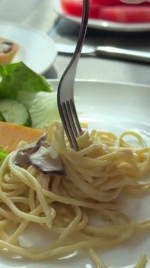 Gri tabakta çıtır pastırmalı, sebzeli ve otlu baharatlı fettuccine spagettisini döndüren yakın çekim çatalı. Yüksek kalite 4k görüntü