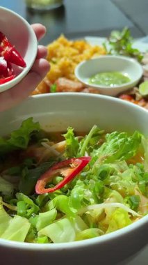 Bir kase wonton eriştesine sambal biberi sosu ekleyen biri, yemeye hazır, Endonezya sokak yemeklerinin zengin lezzetlerini ve baharatlı yemek geleneklerini yakalıyor. Yüksek kalite 4k görüntü