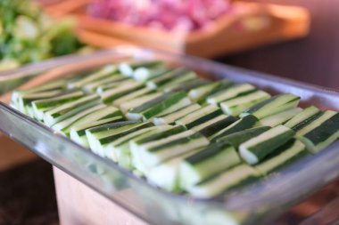 Dilimlenmiş salatalıkları beyaz bir tabakta yakın plan, kırsal ahşap bir iç mekanda servis edilir. Doğal ışık tazeliği artırır. 