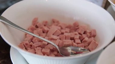 Beyaz zemin üzerinde kaşık tabağıyla pişirilmiş sosis mortadella küpleri.