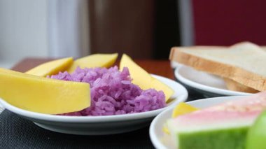 Fıstık ezmesi karışımı, mor pilav ve doğulu mango parçaları. Üzerine hindistan cevizi sütü serpilmiş pilav ve kavrulmuş fıstık. Tabakta servis edilen mangolu pilav. Sonraki yer mango.