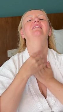 Beyaz çarşafa uzanmış yüz masajı yapan, alnına masaj yapan, ellerini ovuşturan genç, yetişkin bir kadın. Beyaz önlüklü, Avrupalı bir kadın. Yüksek kalite fotoğraf