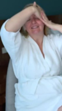 Beyaz çarşafa uzanmış yüz masajı yapan, alnına masaj yapan, ellerini ovuşturan genç, yetişkin bir kadın. Beyaz önlüklü, Avrupalı bir kadın. Yüksek kalite fotoğraf