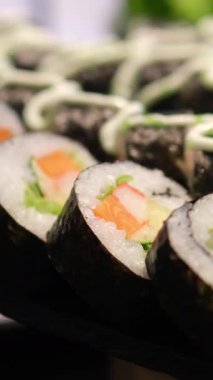 Sushi dürümleri pirinç, yosun, karides, salatalık ve balık yumurtası Japon mutfağının çekici bir sunumunu oluşturuyor. Japon suşisi ve makaralı makro görüntüler. Yüksek kalite 4k