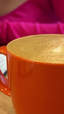 Sıcak latte turuncu fincanlı kız elinde kitapla evde oturmuş kırmızı manikür pembe bluzunu okuyor tanınmayan insanlar ders çalışıyor. Yüksek kalite 4k görüntü