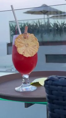 Kırmızı kokteylli plastik bardak ve yüzme havuzunun kenarında çizgili kamış. Yaz tatili havası, güneşli hava, ferahlatıcı su içeceği. Rahatlatıcı tropikal otel atmosferi, tatil