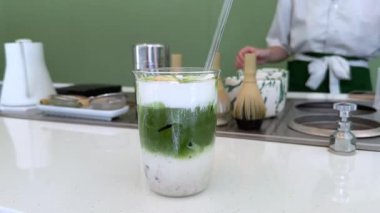 Yeşil kibrit çayı beyaz bir sürahiden beyaz süt içeren cam bardağa dökülüyor. İçki altta belirgin yeşil çay tabakaları ve üstte beyaz süt gösteriyor. - Evet. Yüksek kalite 4k