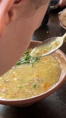 Kız, restoranda çorba, sıvı diyet çorbasını pirinç ve yumurtalarla kokluyor. Çirkin görünümlü bir şekilde masada flatekmek kırıyor. Yüksek kalite 4k görüntü