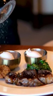 Karabiber şefinin serptiği biber sosu taze ızgara bifteğin dilimlerinin üzerine ahşap kesme tahtasına dökülür. Yemeklere yakın çekim, manzaralı. Yüksek kalite 4k görüntü