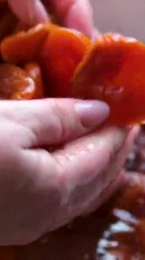 Kadınların eli, beyaz ahşap bir masanın üzerindeki kareli peçeteye yerleştirilmiş bir kaseden kurutulmuş kayısıları alır ve sağlıklı ve lezzetli bir atıştırmalığın tadını çıkarmaya hazırdır. Yüksek kalite 4k görüntü