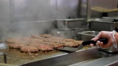 Aşçı, kıymalı burger köftelerini kızgın, siyah ızgara yüzeyinde pişirir, yemekleri yakın plan yapar. Yüksek kalite 4k görüntü