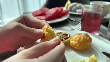 Bir kadın bir masada oturuyor. O, sütlü kahve içecek, kremalı choux pasta ve tatlı çilek yiyecek. Yüksek kalite 4k görüntü