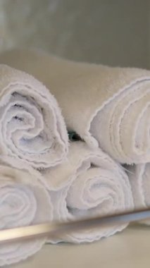 Beyaz çarşaflı düzgün yapılmış bir yatak beyaz havlularla kaplanır ve hoş ve düzenli bir görünüm yaratır. Arka plandaki yumuşak yastıklar odanın davetkar atmosferine katkı sağlıyor..