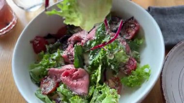 Sağlıklı beslenme konsepti. Masadaki kadın akşam yemeği için sağlıklı sebze salatası hazırlıyor, kadın spatulayla malzemeleri karıştırıyor ve tabağa porsiyon koyuyor. Salatayı tabağa koy.