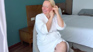 İki taraflı aynanın önünde çarşaf maskesi takan bir kadın. Beyaz bornozlu güzel bir kız elinde kahve ya da çay bardağıyla oturuyor. Rahatla ve rahatla. Önünde bir sürü kozmetik var. .