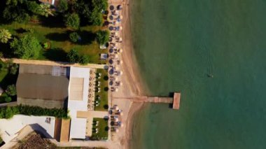 Yunanistan 'da sahil gezisi, yukarıdan manzara, kumdaki şemsiyeler ve güneşlikler, mavi berrak su görülebilir