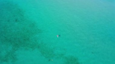 Yunanistan 'ın Korfu adasının kıyısında kırmızı mayo giymiş bir kız mavi suda yüzüyor. Kamera adanın tepesine doğru uçuyor..