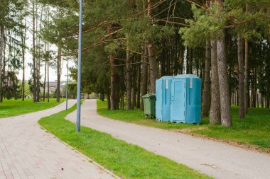 Parktaki mavi biyo-tuvaletler yeşil çöp tenekesinin yanında, parktaki boş çöp kutusu.
