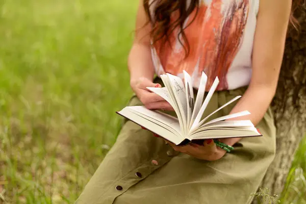 Yeşil çimenlerin üzerinde kitap okuyan bir kadın.