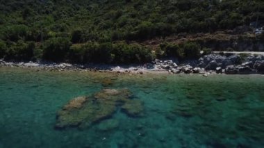 Kıyıdaki mavi okyanus ve yeşil orman. Yükseklerden deniz. Gök mavisi. Scooter okyanusta. Suyun üzerinden uçmak. Deniz kıyısındaki yol. Saf doğa ve su. Kumsalda beyaz kum. 