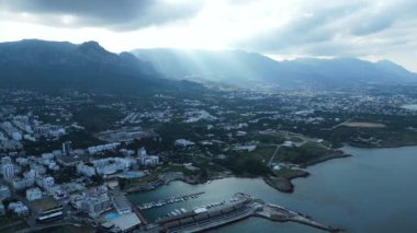 Bir deniz kenti üzerinde bulutlar ve güneş ışınları arasında uçuyor. Güneş ışığındaki dağlar. Yüksek kalite 4k görüntü