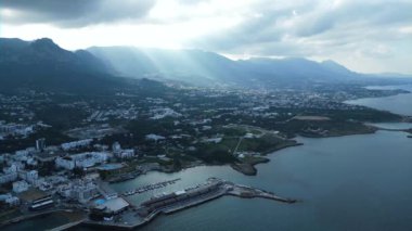 Kıbrıs 'ta bir sahil kasabasının üzerinde uçuyor. Bir liman kasabası. Dağlardaki evler. Limanda yatlar. Bulutların arasından geçen güneş ışınları. Yüksek kalite 4k görüntü
