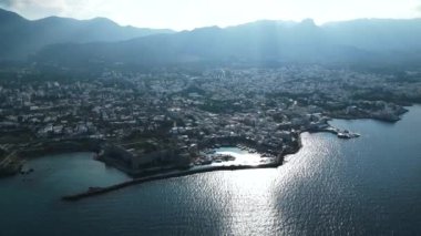 Kıbrıs 'ta bir sahil kasabasının üzerinde uçuyor. Bir liman kasabası. Dağlardaki evler. Limanda yatlar. Bulutların arasından geçen güneş ışınları. Yüksek kalite 4k görüntü