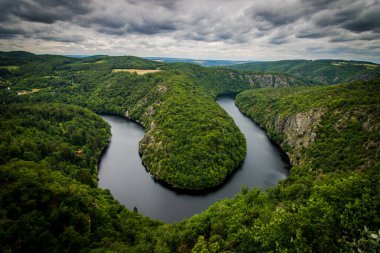 Çek Cumhuriyeti 'nin Maj kenti yakınlarındaki Vltava Nehri' nin manzaralı manzarası, dramatik bulutlu gökyüzü altında yemyeşil ormanlarla çevrili ve manzaralı..