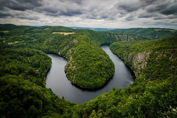 Çek Cumhuriyeti 'nin Maj kenti yakınlarındaki Vltava Nehri' nin manzaralı manzarası, dramatik bulutlu gökyüzü altında yemyeşil ormanlarla çevrili ve manzaralı..