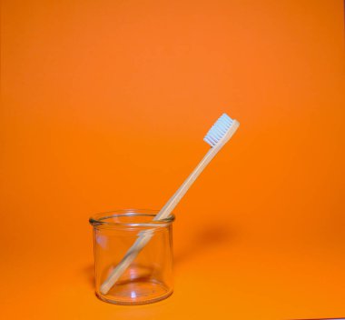 Turuncu arka planda cam bardakta ahşap diş fırçası