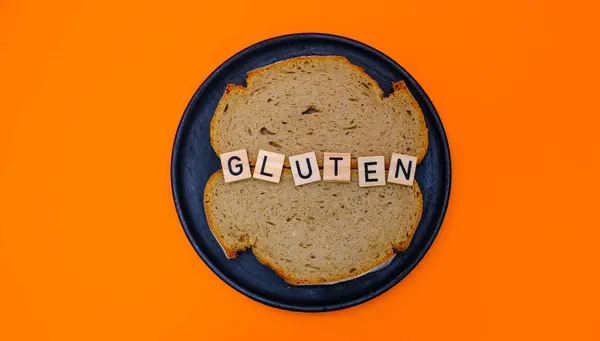 GLUTEN sözcüğü ve un ürünleri, turuncu bir arka planda, ahşap bir siyah plaka üzerinde yakın plan.