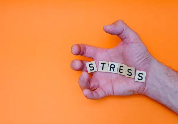 STRESS kelimesi, avucunun içindeki ahşap harflerden felçli parmaklarla yayılmıştır.