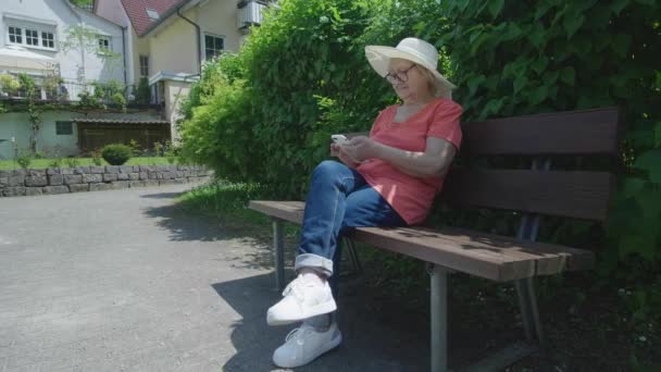 Egy Szemüveges Idős Nézi Telefont Miközben Egy Tavaszi Parkban Egy — Stock videók