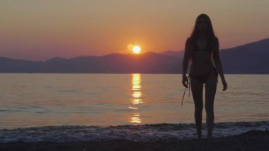 Deniz kıyısındaki ince bir kızın silueti güzel bir gün batımının arka planında dalgalarla