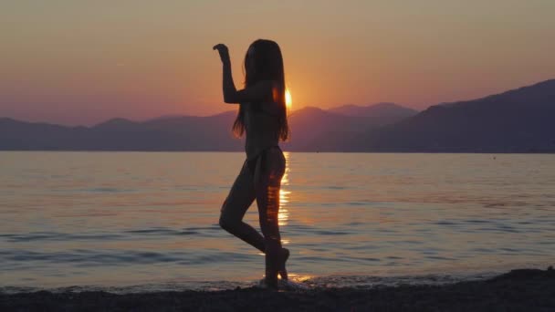 一个身材苗条的女孩在海滨被美丽的夕阳西下的波浪映衬的轮廓 — 图库视频影像