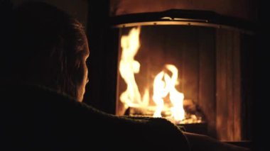 Kız şöminenin yanında oturuyor ve ateşe bakıyor.
