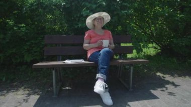 Gözlüklü yaşlı bir kadın bahar parkında otururken çay içer. Doğada çay içen bir emeklinin portresi. Boş zaman konsepti.