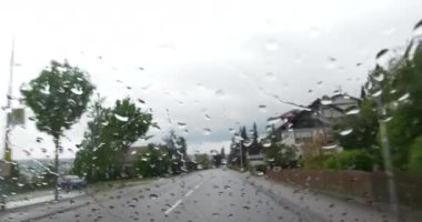 Bir arabanın ön camından yol manzarası, camdan aşağı akan yağmur damlaları.