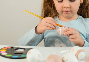 Paskalya yumurtası avındaki çocuklar. Çocuklar yumurta boyar. Tavşan kulaklı mutlu küçük bir kızın portresi masaya oturmuş ve Paskalya için yumurta boyuyor.