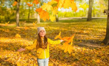 Sonbahar parkında renkli, parlak sonbahar yaprakları atan bir kız.