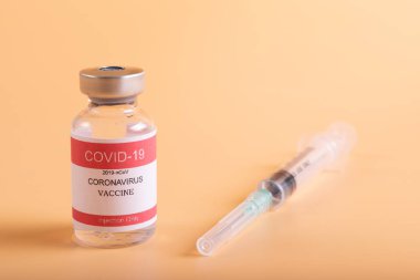 Turuncu pastel arka planda covid aşı ve şırınga