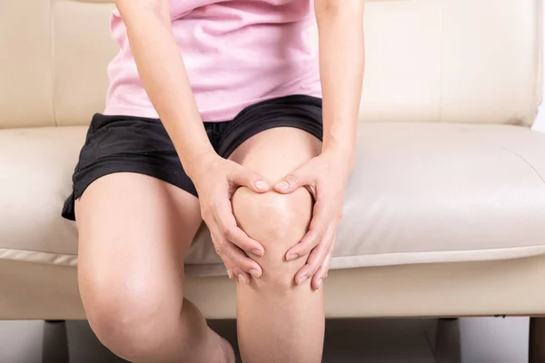 Kanepede oturan ve diz ağrısı çeken genç bir kadın. Sağlık ve Tıp Konsepti.